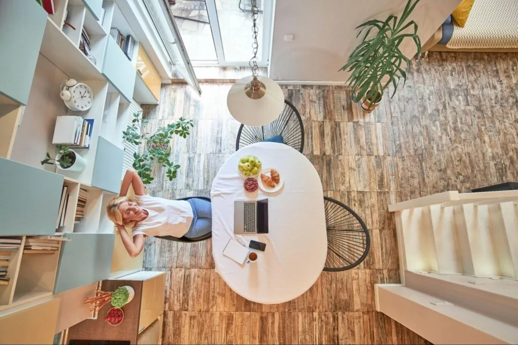 Top view of a woman relaxing in a bright compact dining area with a laptop and breakfast on the table, illustrating a tidy, clutter-free small home.